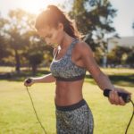 ¡Entrena en el parque y ponte en forma! Fit young woman with jump rope in a park